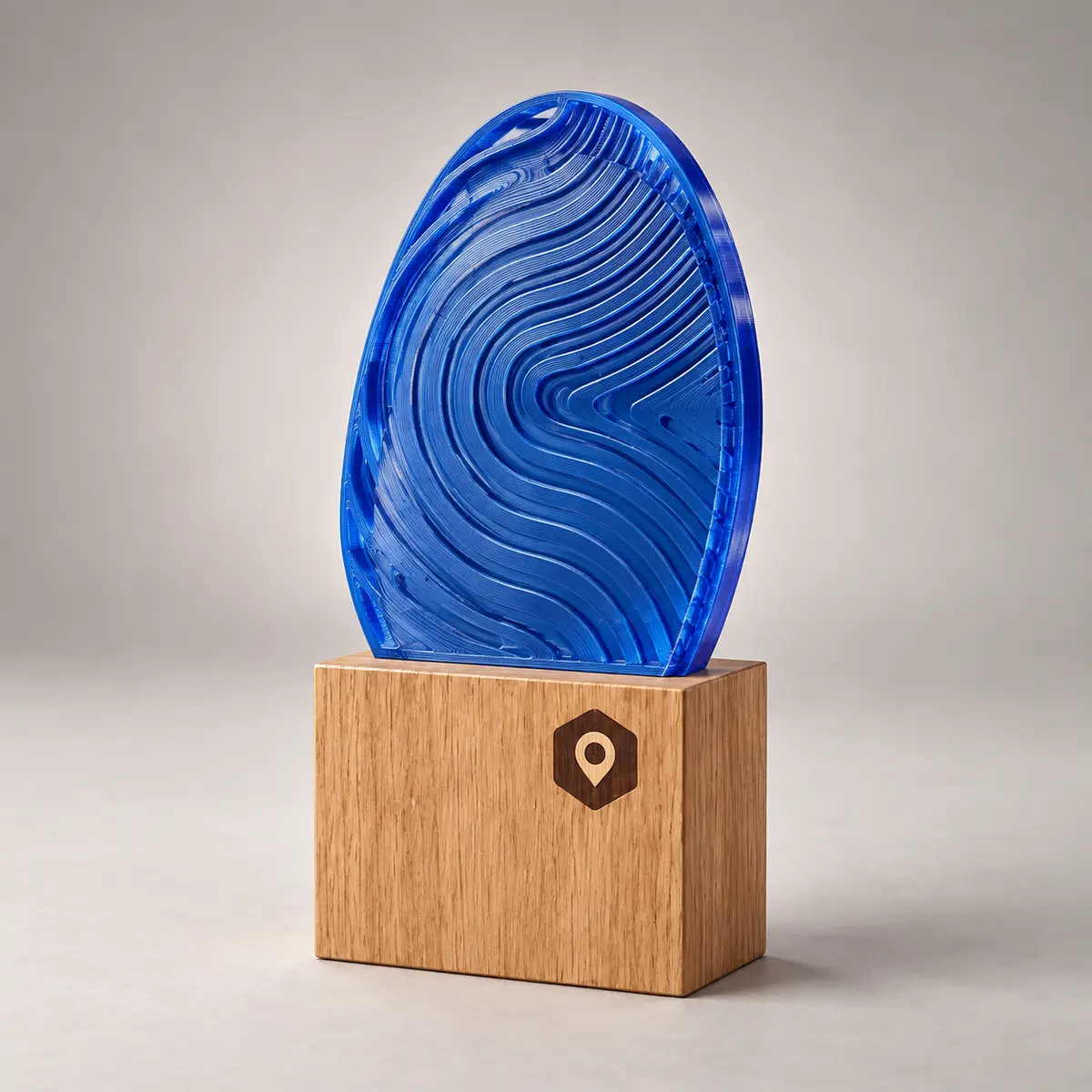 Peça 3D oval azul translúcida com ondas em relevo, sobre base de madeira com logo gravada